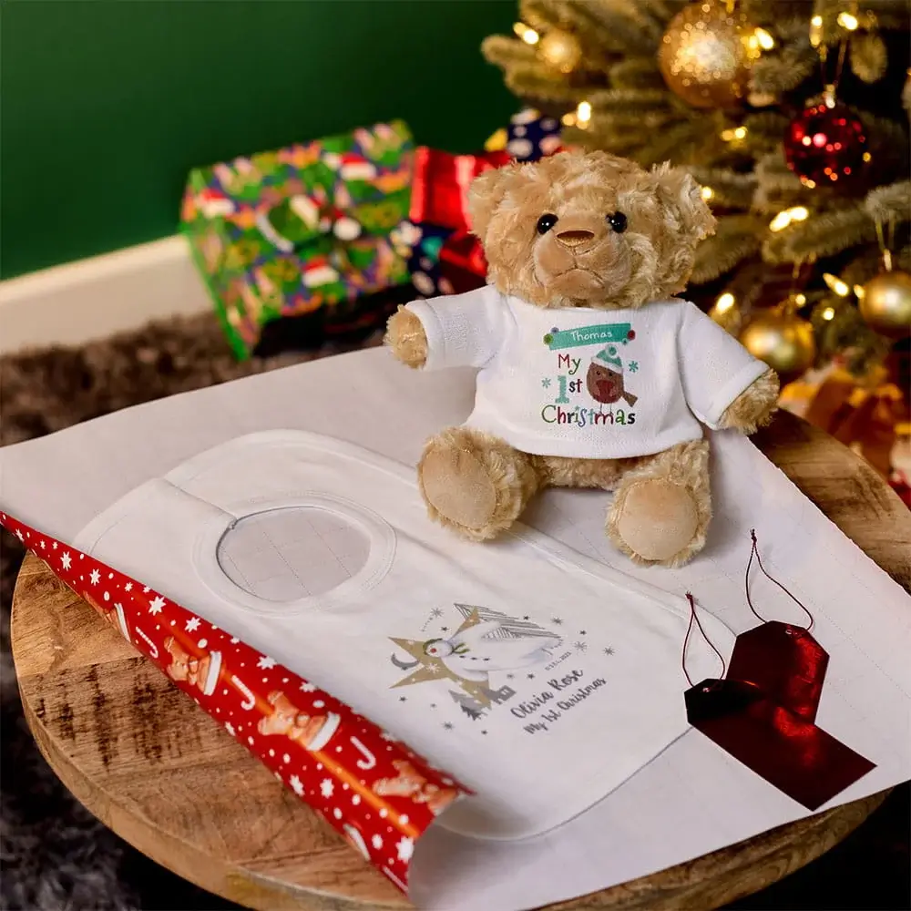 Personalised Christmas keepsake set featuring a teddy bear in a festive T-shirt, a baby handprint kit, gift wrapping paper, and Christmas decorations by a Christmas tree. Personalised Christmas keepsake set featuring a teddy bear in a festive T-shirt, a baby handprint kit, gift wrapping paper, and Christmas decorations by a Christmas tree.